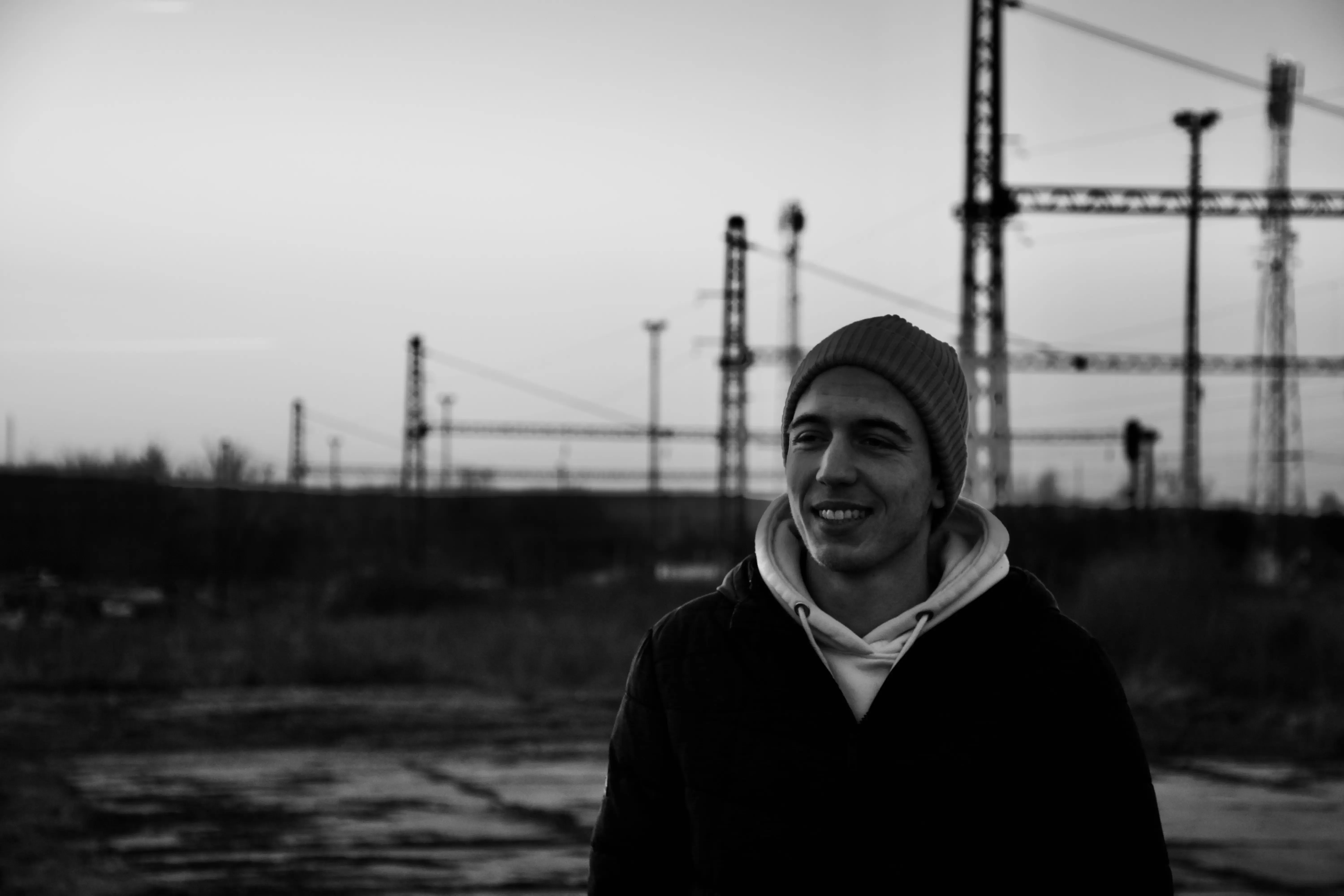 Black-and-white portrait of Barabás Ákos in front of railway gantries at dusk